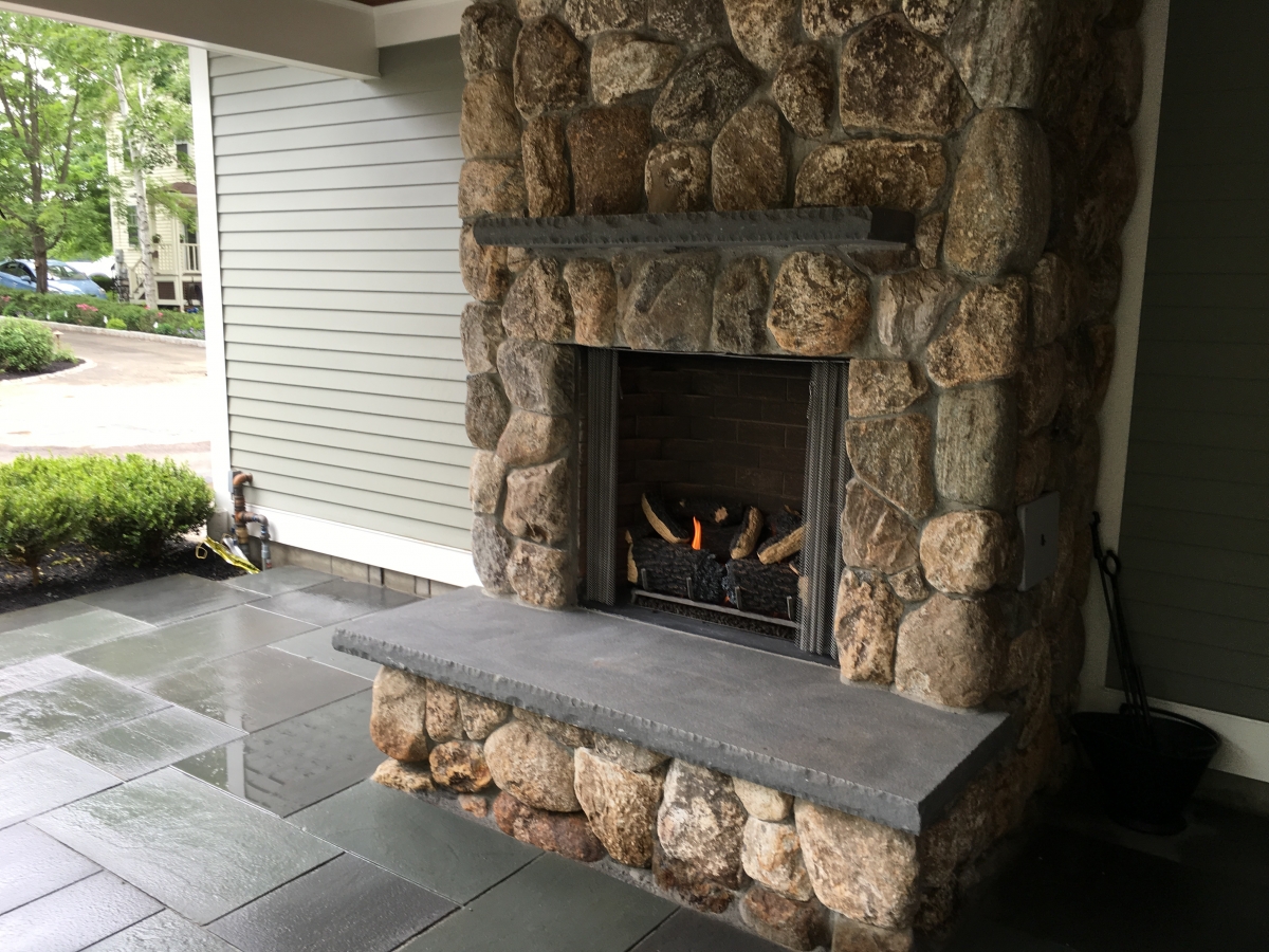 outdoor gas fireplace with stone surround and black stone mantel